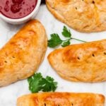 Four golden-brown easy taco pockets are arranged on a light surface with green cilantro leaves.