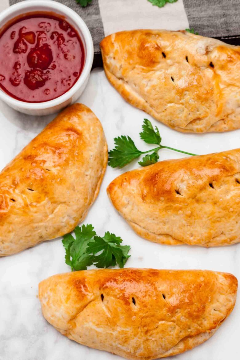 Four golden-brown easy taco pockets are arranged on a light surface with green cilantro leaves. 