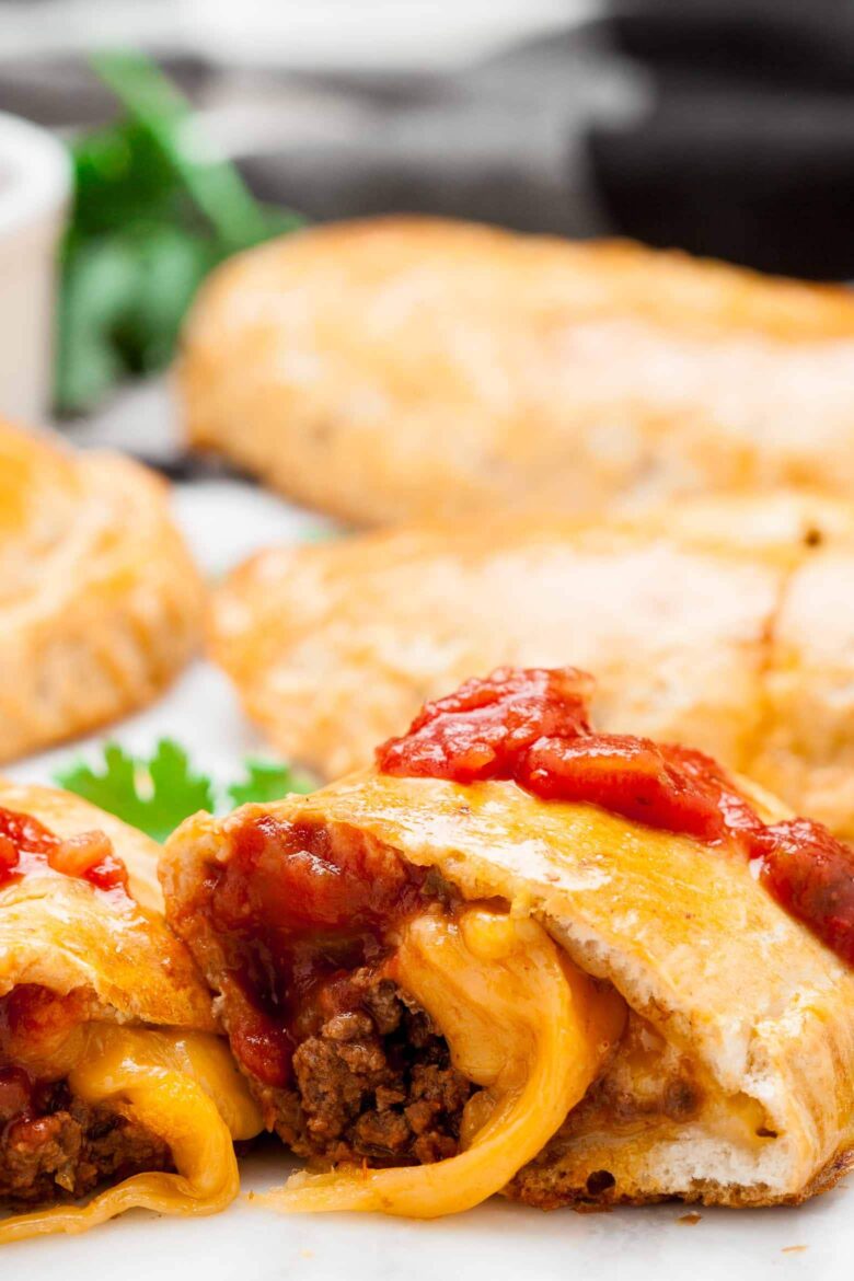 A close-up of a easy taco pockets cut in half, revealing ground beef and melted cheese filling, topped with tomato salsa.
