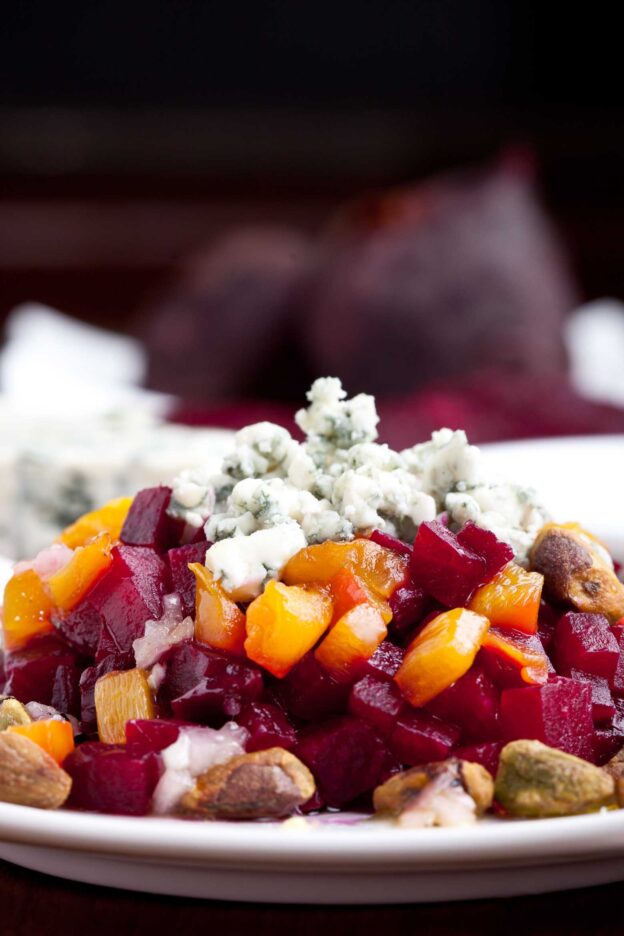 A close-up of a plate featuring a beet salad with diced roasted peppers, crumbled blue cheese, and pistachios.
