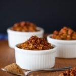 Three white ramekins filled with brown sugar baked beans topped with bacon bits on a wooden surface.