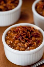 A white ramekin filled with brown sugar baked beans topped with crumbled bacon.