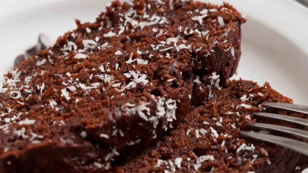 Two slices of chocolate chip zucchini bread topped with shredded coconut on a white plate with a fork.