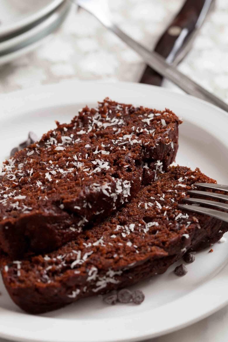 Two slices of chocolate chip zucchini bread topped with shredded coconut on a white plate with a fork.