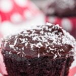 A close-up of a chocolate zucchini cupcake with orange-chocolate frosting and shredded coconut on top.