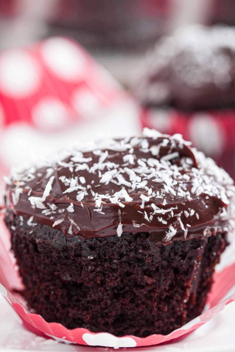 A close-up of a chocolate zucchini cupcake with orange-chocolate frosting and shredded coconut on top.