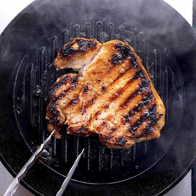 Pork chops being grilled with beautifully grill marks on top.