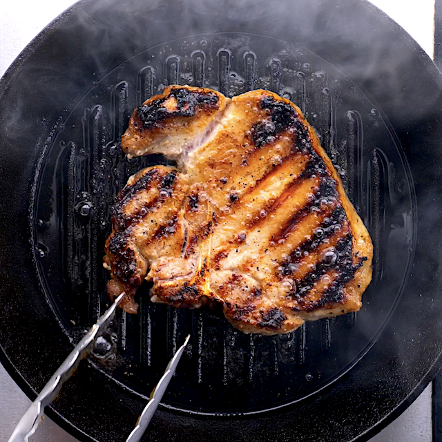 Pork chops being grilled with beautifully grill marks on top.