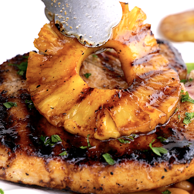 Grilled pineapple rings being served on top of grilled pork chops.