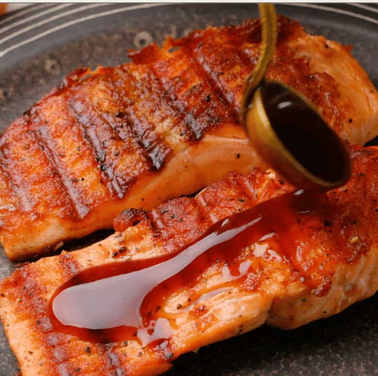 teriyaki sauce being poured onto grilled salmon fillets. 
