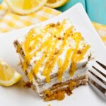 A slice of layered lemon icebox cake topped with whipped cream and lemon curd, served on a white plate.