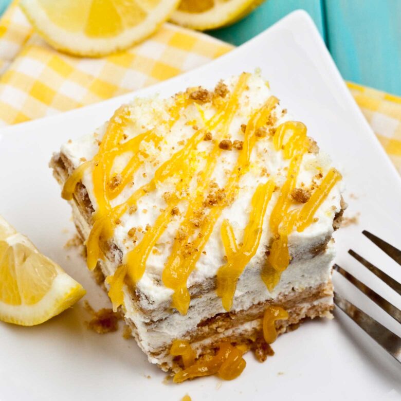 A slice of layered lemon icebox cake topped with whipped cream and lemon curd, served on a white plate.