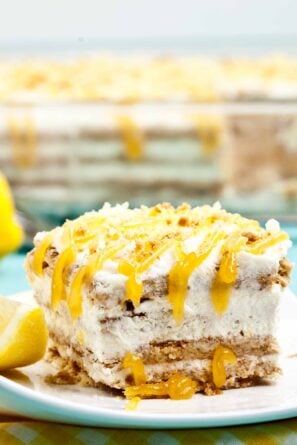 A slice of layered lemon icebox cake with graham cracker crust and whipped cream topping, drizzled with lemon curd.