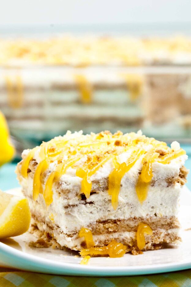 A slice of layered lemon icebox cake with graham cracker crust and whipped cream topping, drizzled with lemon curd.