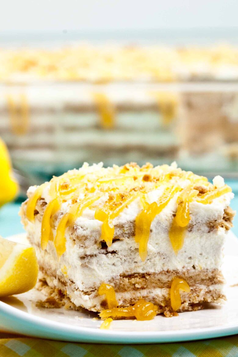 A slice of layered lemon icebox cake with graham cracker crust and whipped cream topping, drizzled with lemon curd.