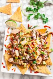 A plate of BBQ chicken nachos topped with diced vegetables, pineapple chunks, cheese, and fresh cilantro.
