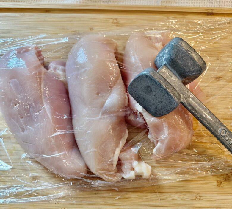 Chicken breast being pounded to an even thickness to make healthy chicken Alfredo.