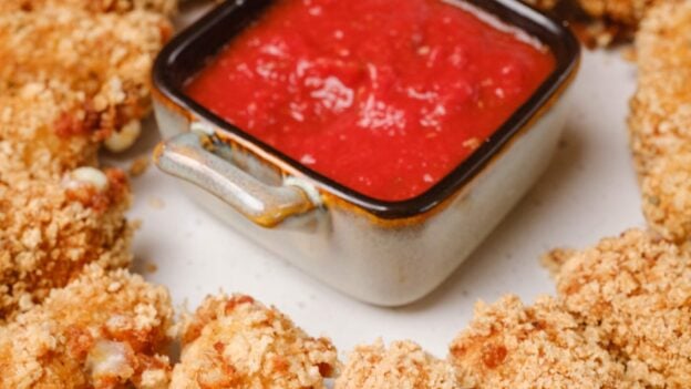 A plate of extra crispy homemade mozzarella sticks served around a delicious dipping sauce.