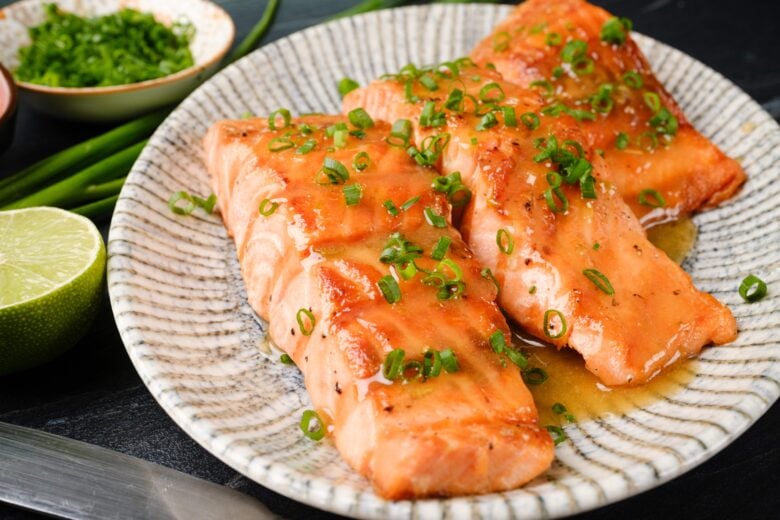 Grilled honey glazed salmon garnished with chopped green onions on a white patterned plate.