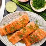 A plate with three grilled honey-glazed salmon fillets garnished with chopped green onions.