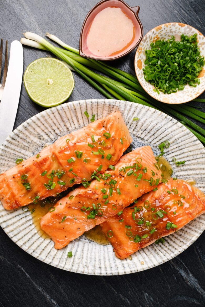 A plate with three grilled honey-glazed salmon fillets garnished with chopped green onions.