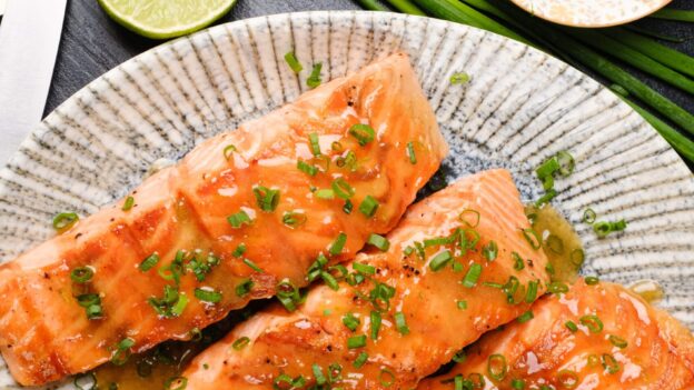 A plate with three grilled honey-glazed salmon fillets garnished with chopped green onions.