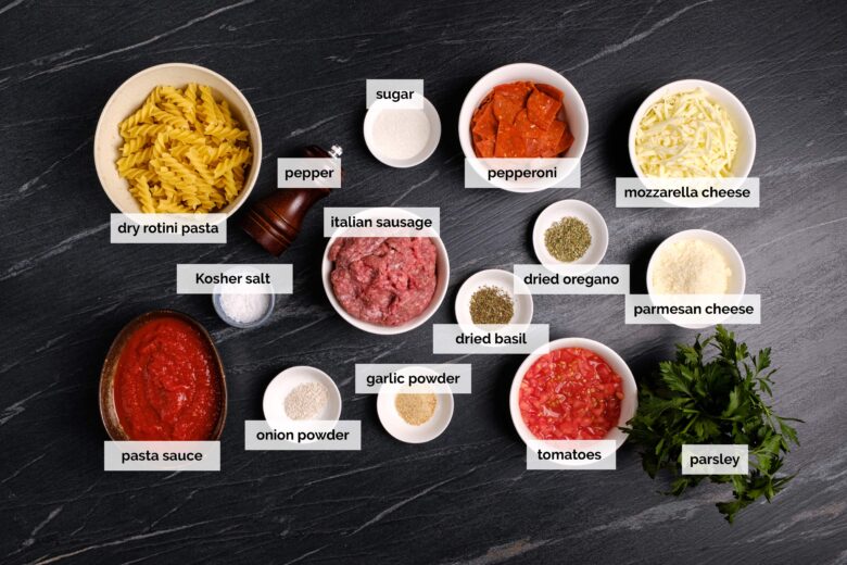 Overhead shot of ingredients to make one pot pizza pasta on a dark surface.