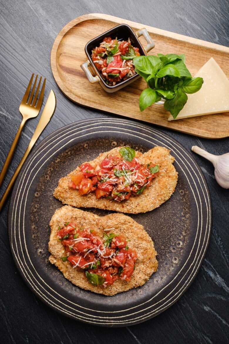 Overhead shot of a plate with two parmesan crusted chicken, topped with tomato bruschetta.