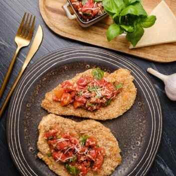 Overhead shot of a plate with two parmesan crusted chicken, topped with tomato bruschetta.