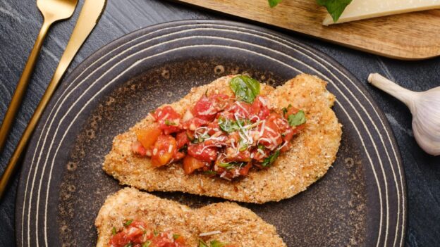 Overhead shot of a plate with two parmesan crusted chicken, topped with tomato bruschetta.