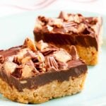 Two peanut butter chocolate crispy bars with a crunchy base and chopped peanut butter cups on top.