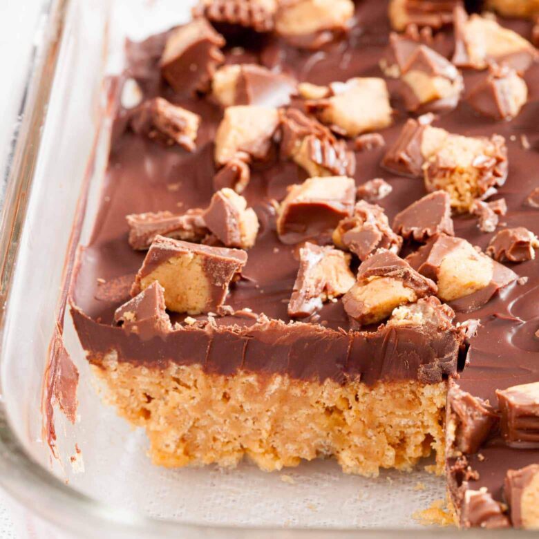 Peanut butter chocolate crispy bars in a glass baking dish with chopped peanut butter cups on top.