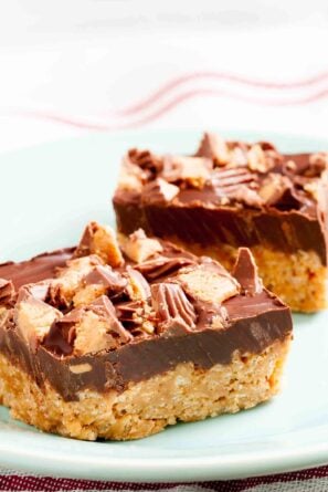Two peanut butter chocolate crispy bars with a crunchy base and chopped peanut butter cups on top.