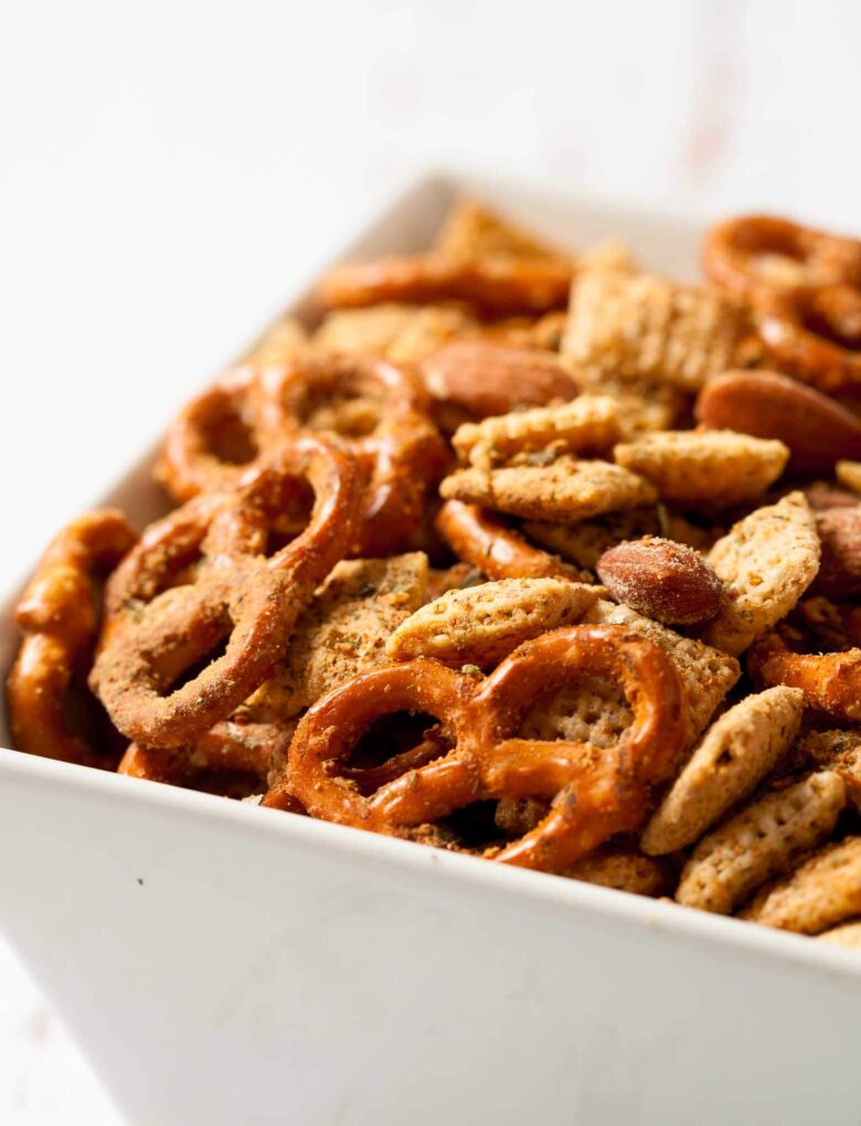 A close-up of a bowl filled with a homemade Gluten Free Chex Mix, including pretzels, almonds, and cereal pieces.
