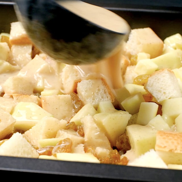 Bread pudding mixture being poured over cubed bread, apples, and raisins to make apple bread pudding.