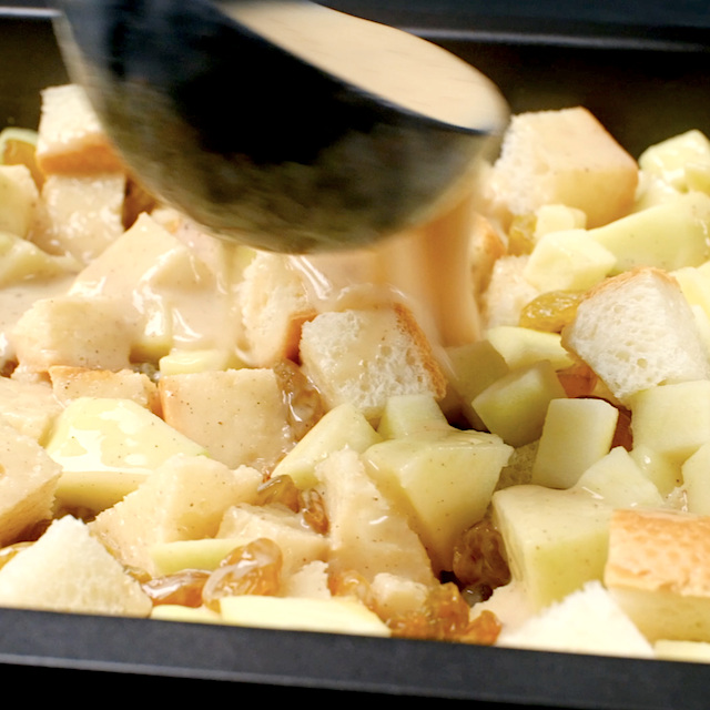 Bread pudding mixture being poured over cubed bread, apples, and raisins to make apple bread pudding.
