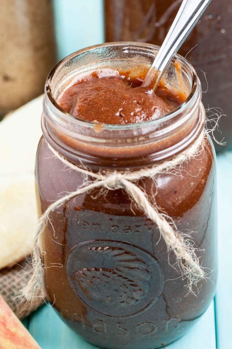 A jar of homemade apple butter with a spoon inside.