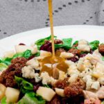 Apple pecan salad being drizzled with homemade dressing before serving.