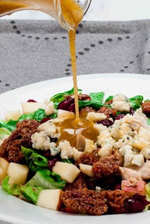 Apple pecan salad being drizzled with homemade dressing before serving.