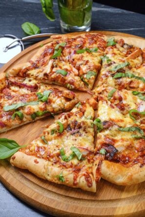 A freshly baked BBQ chicken pizza cut into six slices, placed on a wooden serving board.