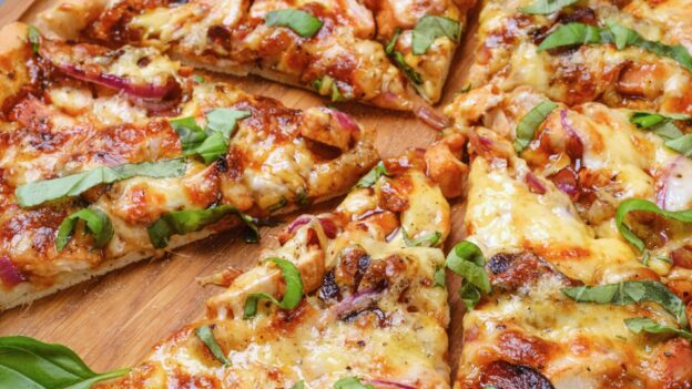 A freshly baked BBQ chicken pizza cut into six slices, placed on a wooden serving board.