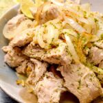 A bowl of shredded Cuban mojo pork drizzled with mojo sauce and garnished with sautéed onions.