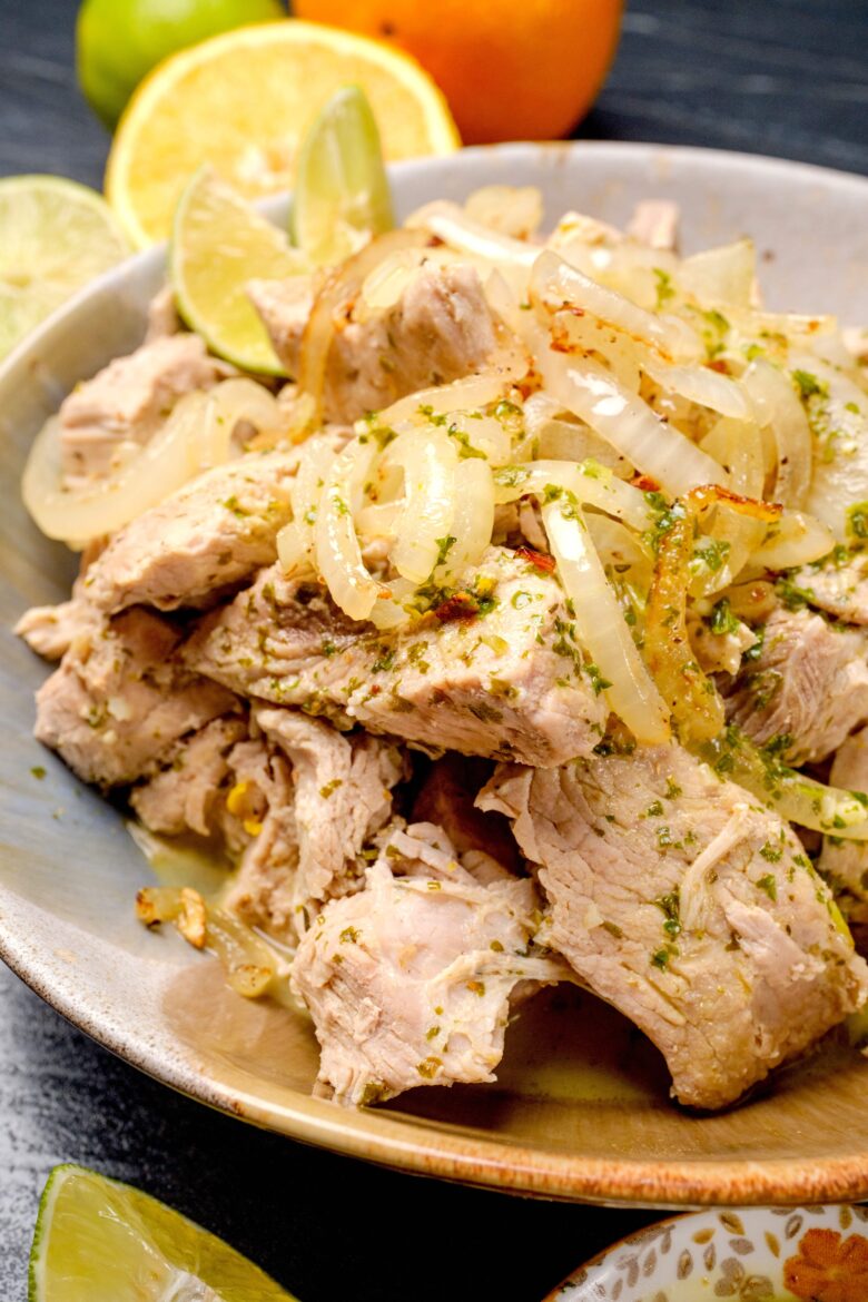 A bowl of shredded Cuban mojo pork drizzled with mojo sauce and garnished with sautéed onions.