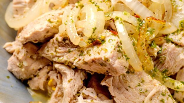 A bowl of shredded Cuban mojo pork drizzled with mojo sauce and garnished with sautéed onions.