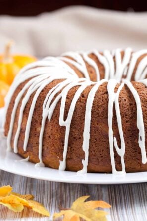 Pumpkin bundt cake with cream cheese glaze on top on a white plate with fall leaves around it.