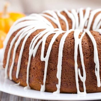 Pumpkin bundt cake with cream cheese glaze on top on a white plate with fall leaves around it.