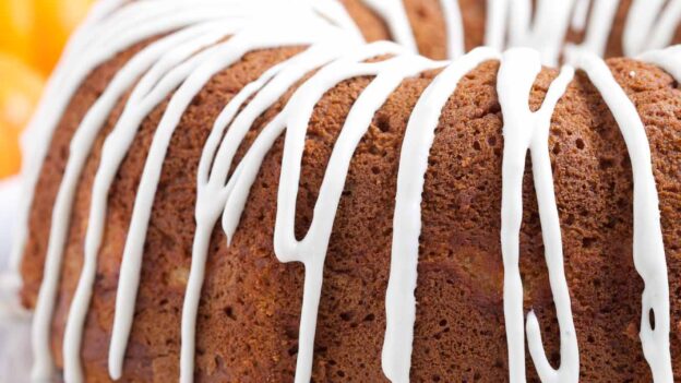 Pumpkin bundt cake with cream cheese glaze on top on a white plate with fall leaves around it.