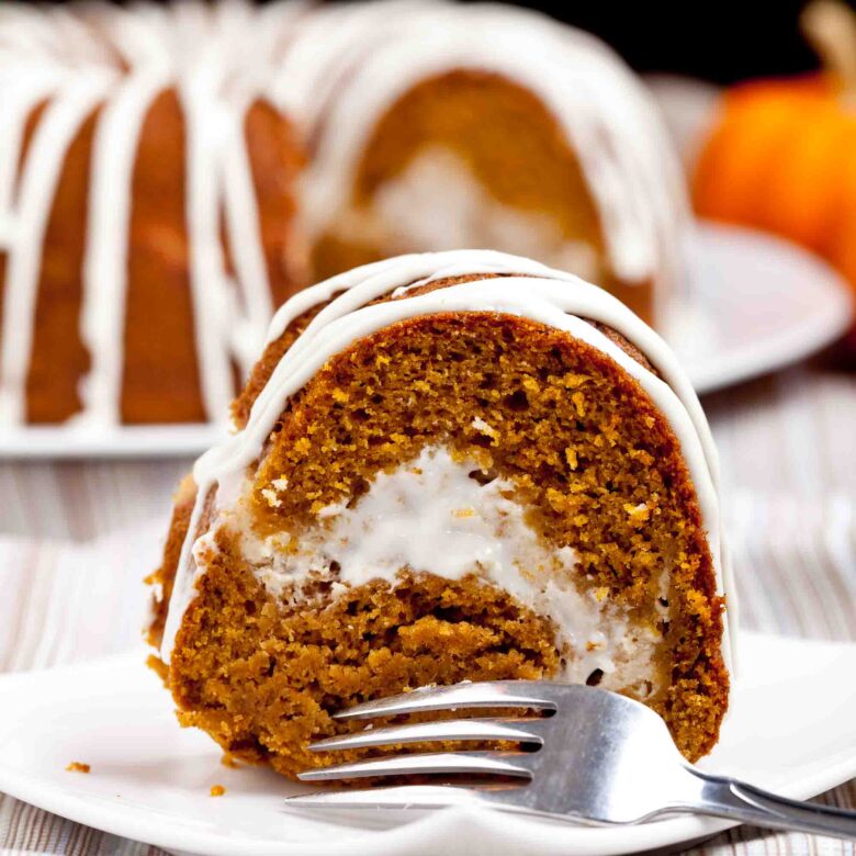 Close up shot of a slice of pumpkin bundt cake with cream cheese frosting, with a fork on the side.