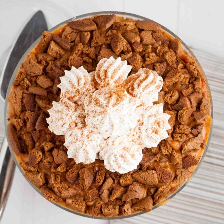 Overhead shot of pumpkin trifle with crumbled gingersnaps and whipped cream on top that's dusted with ground cinnamon.
