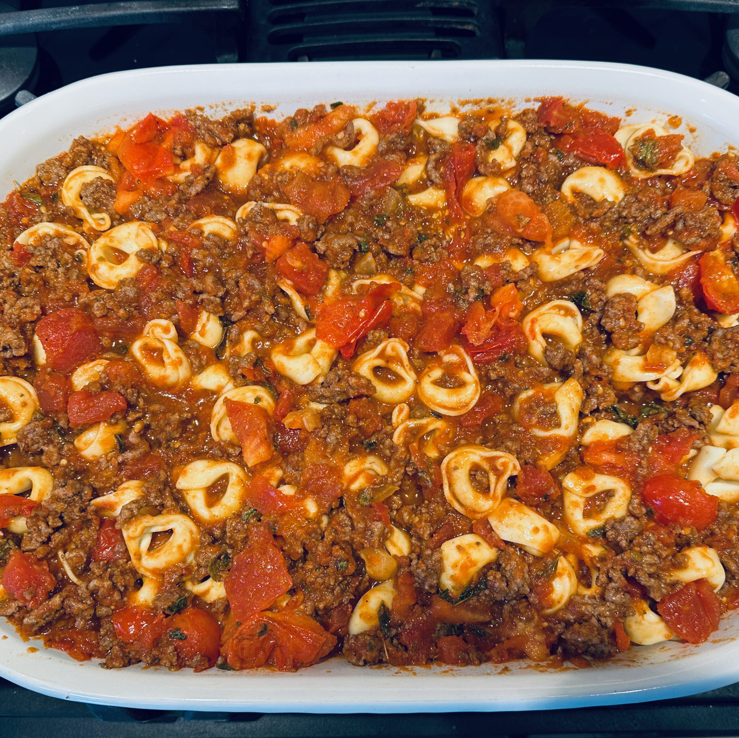 Layers of ground beef and pasta sauce mixture and cheesy tortellini in a casserole pan to make cheesy baked tortellini.